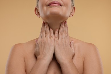 Mature woman touching her neck on beige background, closeup