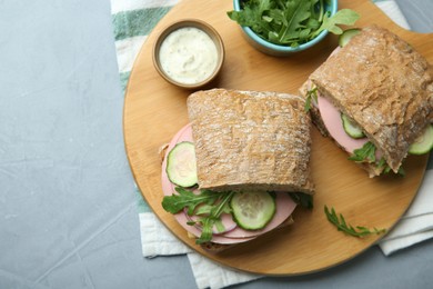 Photo of Tasty sandwiches with boiled sausage, cucumber, arugula and sauce on grey table, top view. Space for text