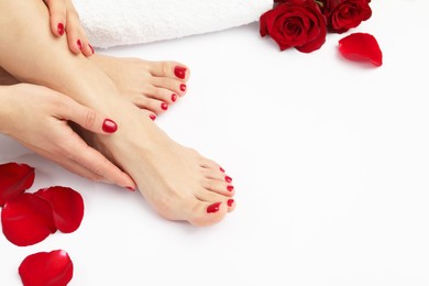 Photo of Woman with stylish red toenails after pedicure procedure and rose flowers on white background, closeup. Space for text