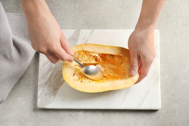 Photo of Woman scraping flesh of spaghetti squash with spoon on table, top view