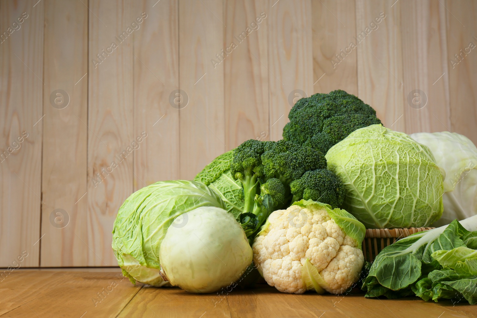 Photo of Many different types of fresh cabbage on wooden table. Space for text