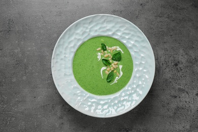 Photo of Plate of healthy green soup with fresh spinach on grey table, top view