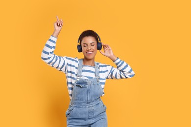 Happy young woman in headphones dancing on orange background