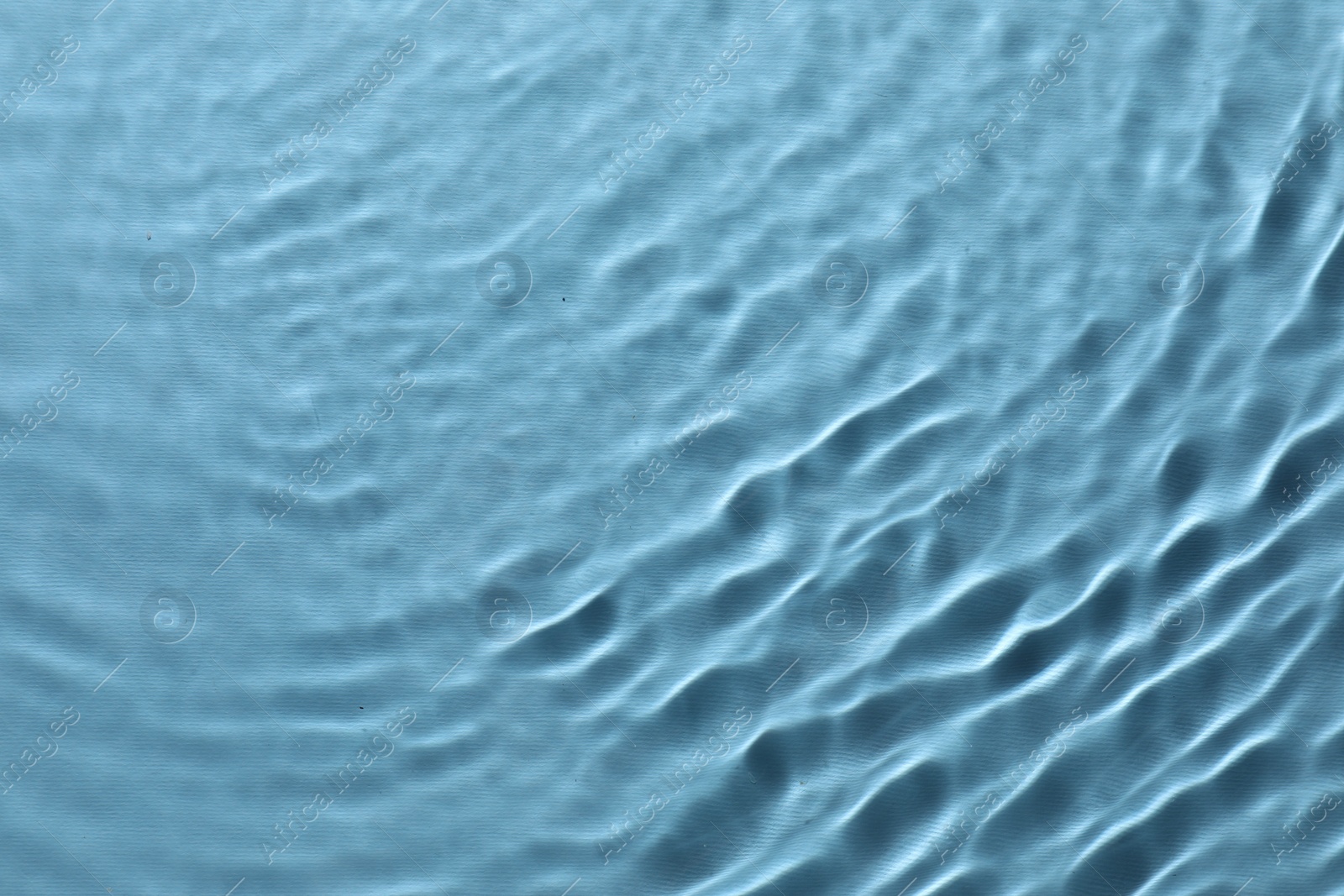 Photo of Rippled surface of clear water on light blue background, top view