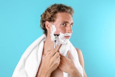 Handsome young man shaving on color background