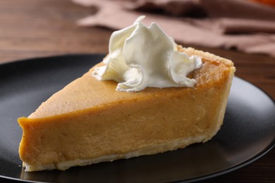 Piece of delicious pumpkin pie with whipped cream on table, closeup