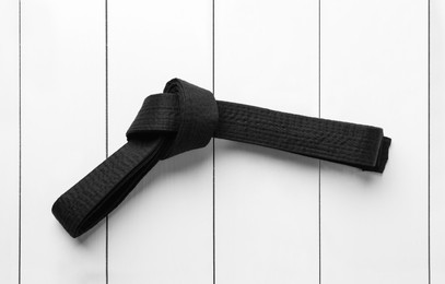 Photo of Tied black belt on white wooden background, top view. Oriental martial arts