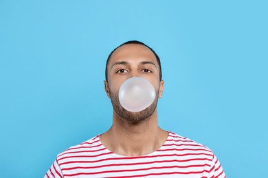 Photo of Portrait of young man blowing bubble gum on light blue background