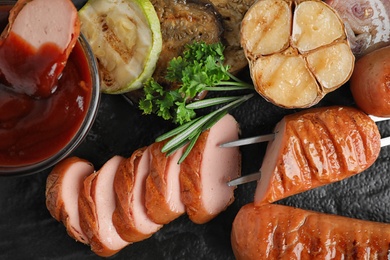 Photo of Closeup view of delicious grilled sausages and vegetables on dark table, flat lay