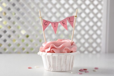 Photo of Delicious cupcake with pink cream and Girl topper for baby shower on white table