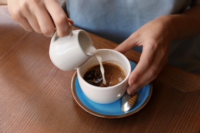 Photo of Woman adding milk to fresh aromatic coffee at table, closeup