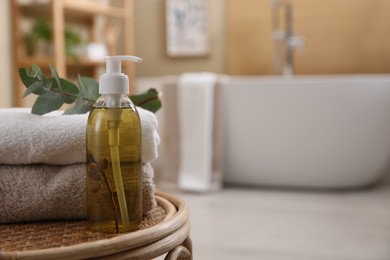 Photo of Dispenser of liquid soap, clean towels and eucalyptus branch on wicker stool in bathroom. Space for text