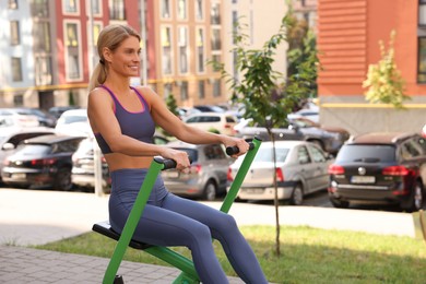 Happy woman training on rowing machine at outdoor gym, space for text
