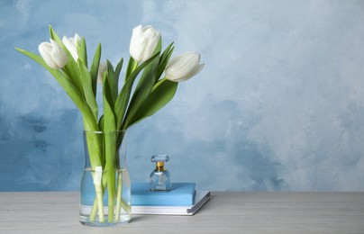 Beautiful white tulips, notebooks and perfume on wooden table against light blue background, space for text