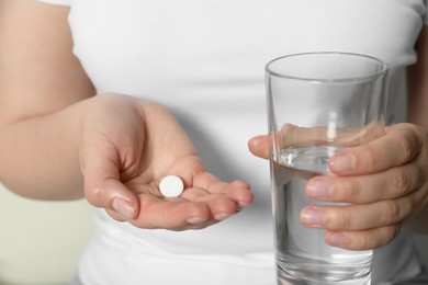 Photo of Woman holding glass of water and pill, closeup