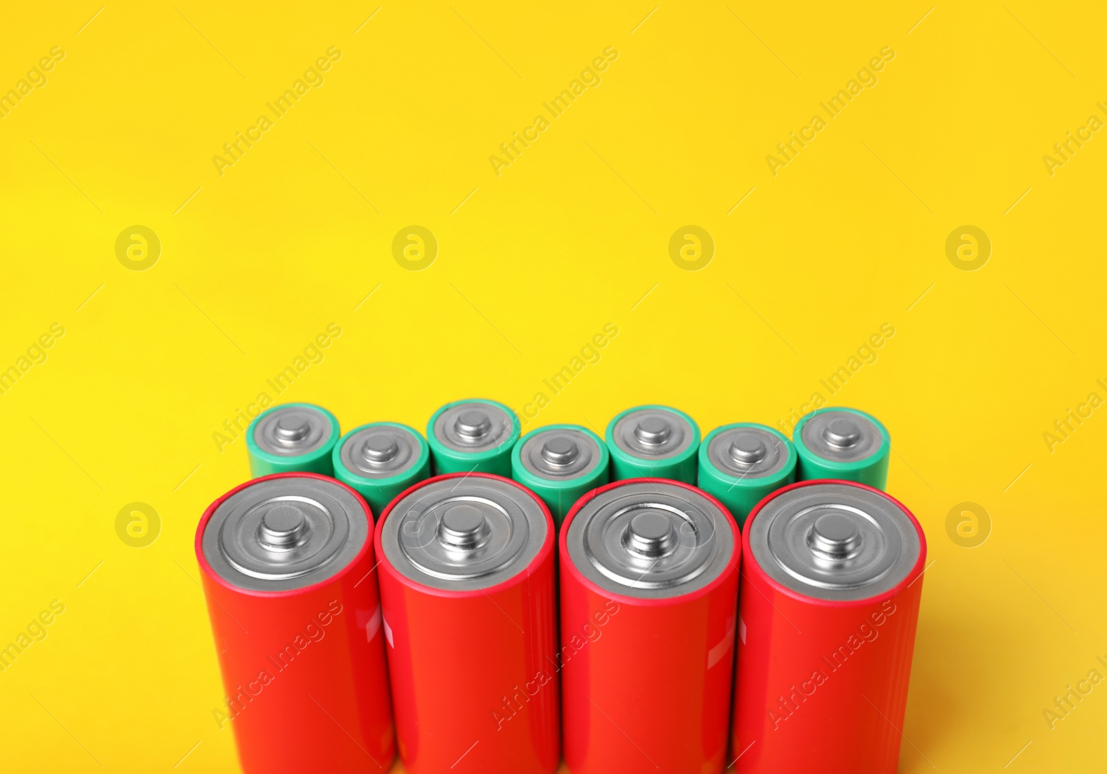 Photo of Batteries of different sizes on yellow background. Space for text