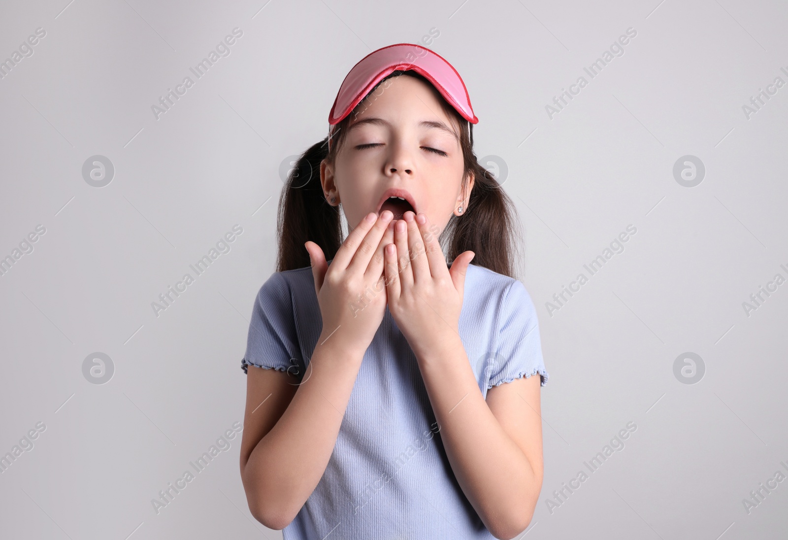 Photo of Tired little girl with sleep mask yawning on light background