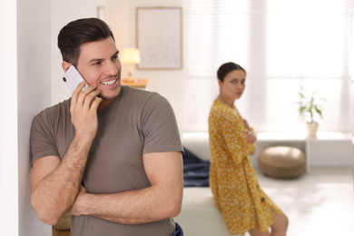 Photo of Man preferring talking on phone over spending time with his girlfriend at home. Jealousy in relationship