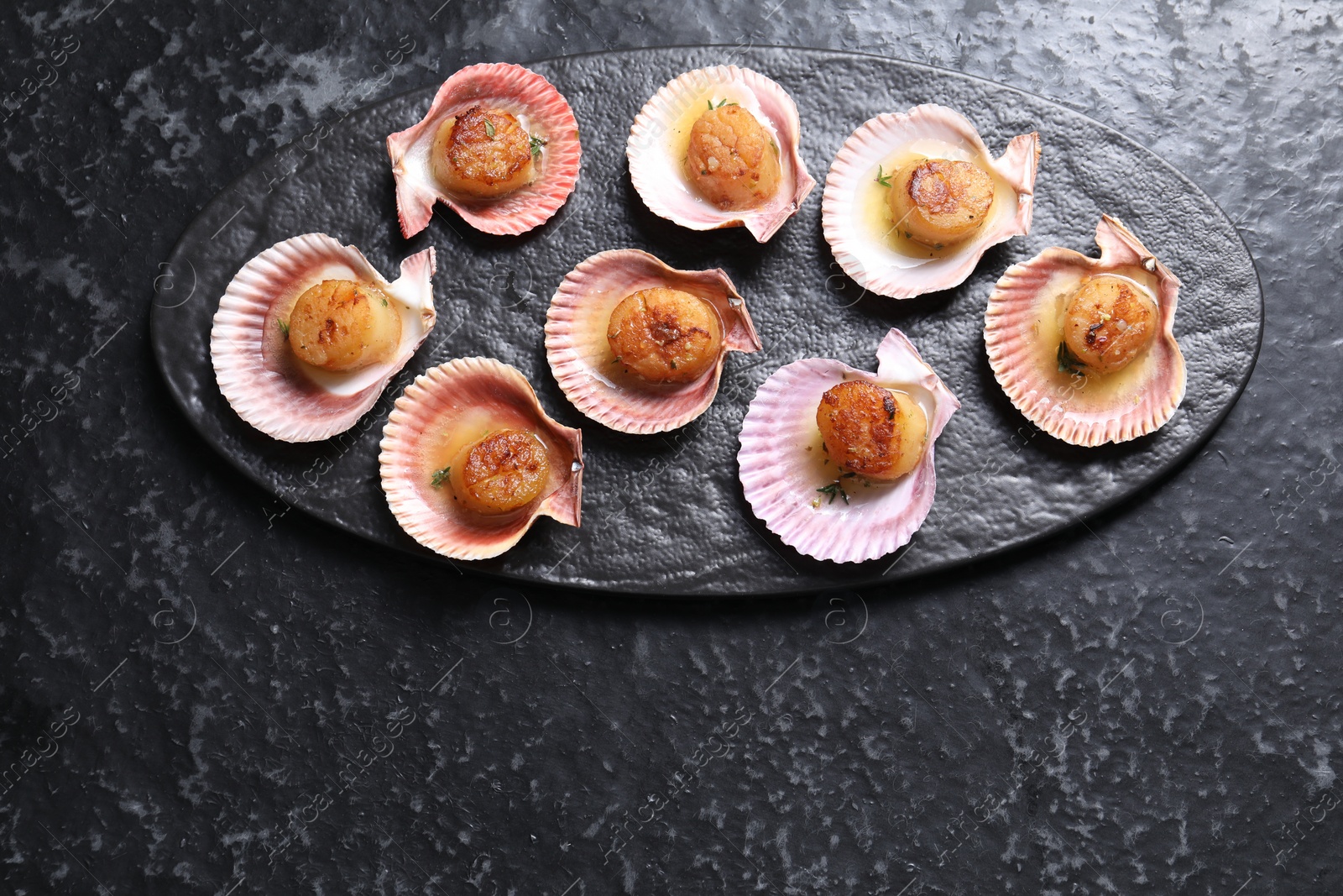 Photo of Delicious fried scallops in shells on black table, top view