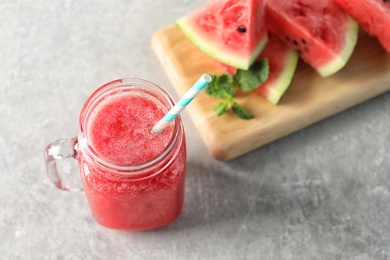 Photo of Tasty summer watermelon drink in mason jar and board with sliced fruit on table