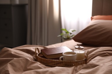 Cup of hot coffee and books on bed with stylish linens in room