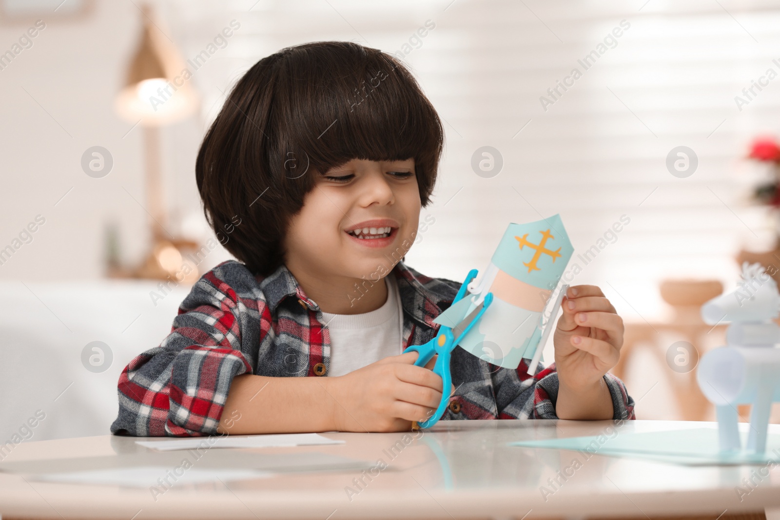 Photo of Cute little boy making paper Saint Nicholas toy at home