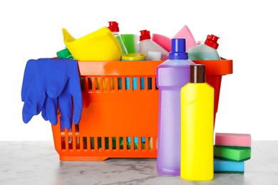 Shopping basket with different detergents on marble table against white background