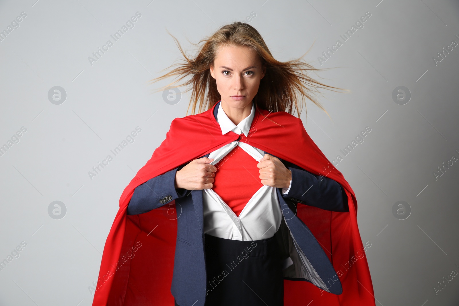 Photo of Confident businesswoman wearing superhero costume under suit on light grey background