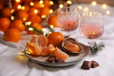 Delicious ripe tangerines, chocolates, festive lights and glasses of wine on white bedsheet