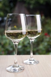 Glasses of white wine served on wooden table outdoors