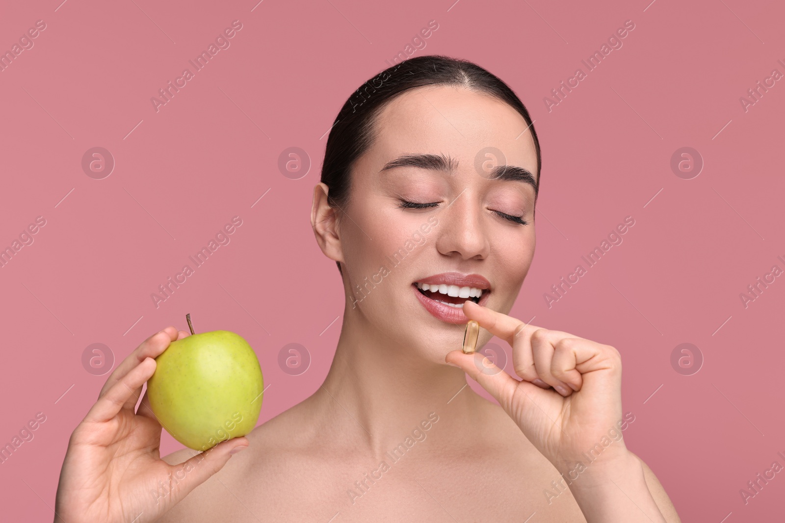 Photo of Beautiful young woman with vitamin pill and apple on pink background