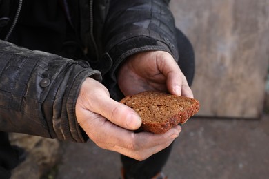 Photo of Poor homeless man holding piece of bread outdoors, closeup