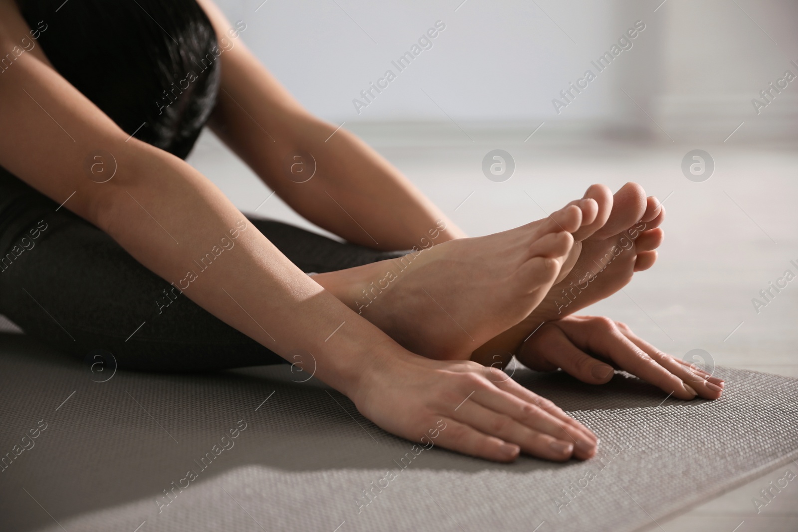 Photo of Young woman practicing seated forward bend asana in yoga studio, closeup. Paschimottanasana pose