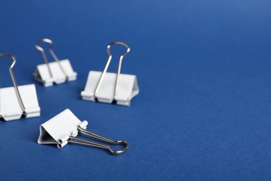 Photo of White binder clips on blue background, closeup. Space for text