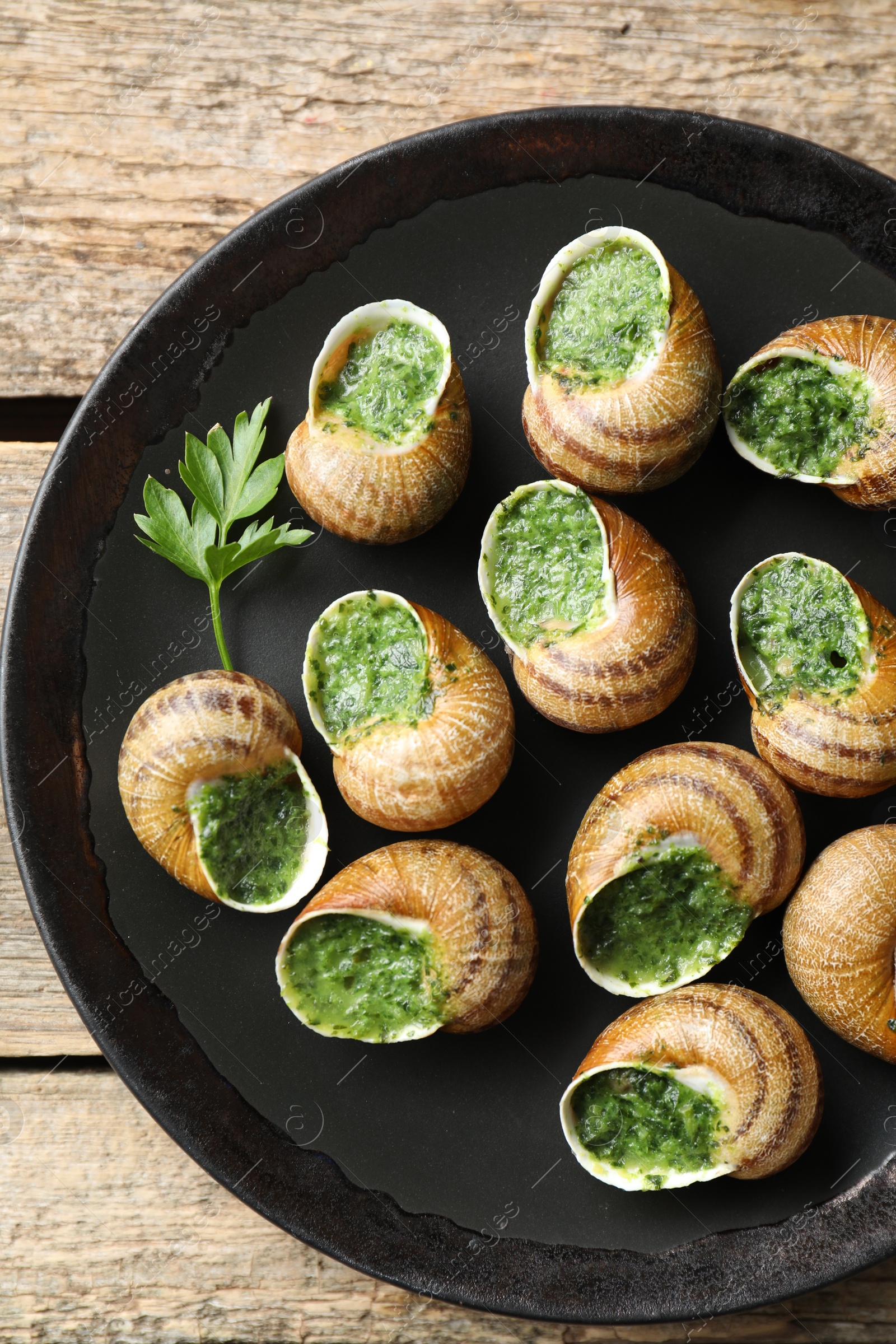 Photo of Delicious cooked snails with parsley on wooden table, top view