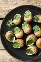 Photo of Delicious cooked snails with parsley on wooden table, top view