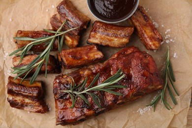 Photo of Tasty roasted pork ribs served with sauce and rosemary on table, top view