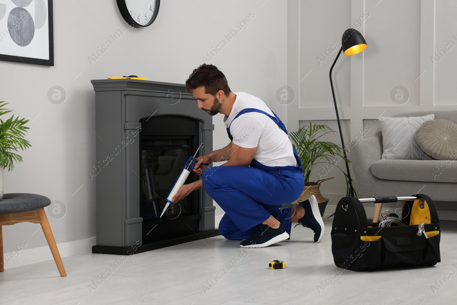 Photo of Professional technician sealing electric fireplace with caulk near white wall in room