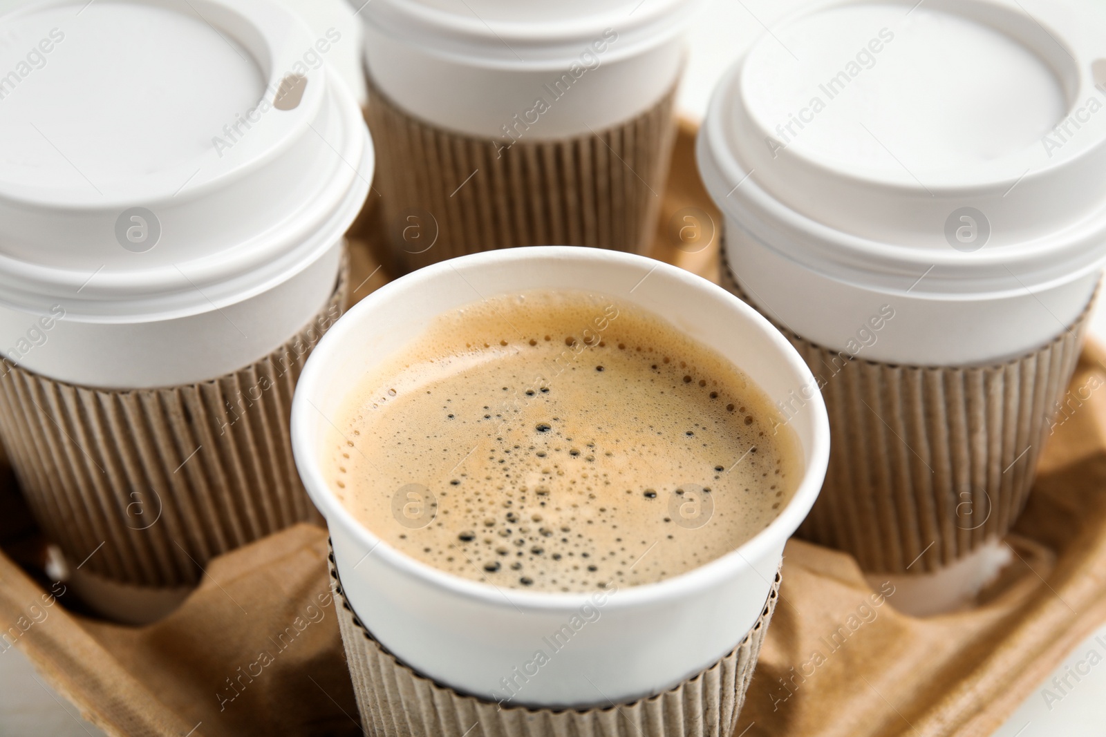 Photo of Takeaway paper coffee cups with sleeves in cardboard holder, closeup