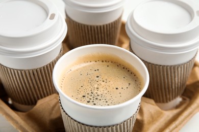 Photo of Takeaway paper coffee cups with sleeves in cardboard holder, closeup