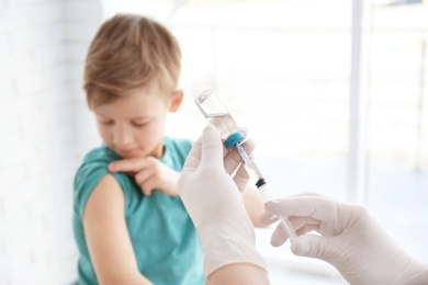 Doctor filling syringe with medicine and child on background. Vaccination day