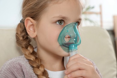 Little girl using nebulizer for inhalation indoors, closeup