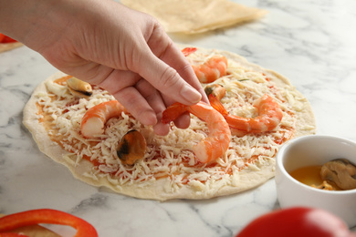Photo of Woman adding shrimp to seafood pizza at white marble table, closeup