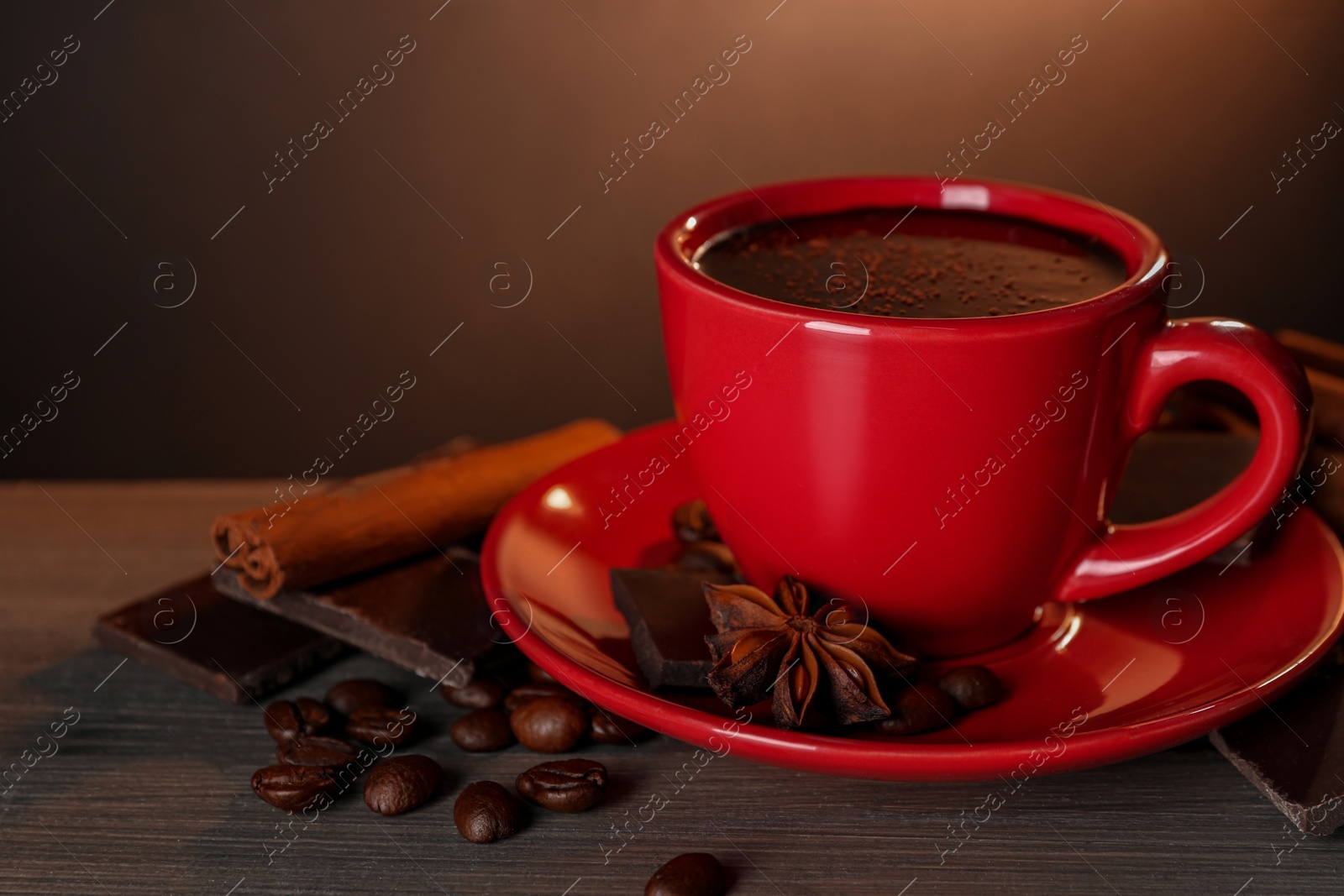 Photo of Cup of delicious hot chocolate, spices and coffee beans on wooden table. Space for text