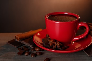 Cup of delicious hot chocolate, spices and coffee beans on wooden table. Space for text