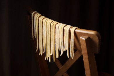 Photo of Homemade pasta drying on chair against dark background, closeup