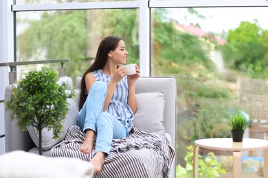 Photo of Young beautiful woman drinking morning coffee near window at home