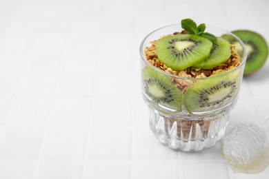 Photo of Delicious dessert with kiwi and muesli on white table, closeup. Space for text