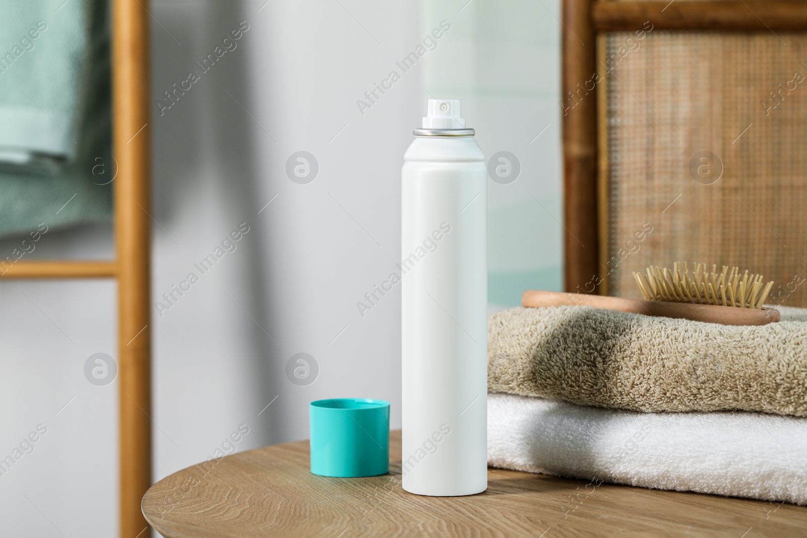 Photo of Bottle of dry shampoo, towels and hairbrush on wooden table indoors