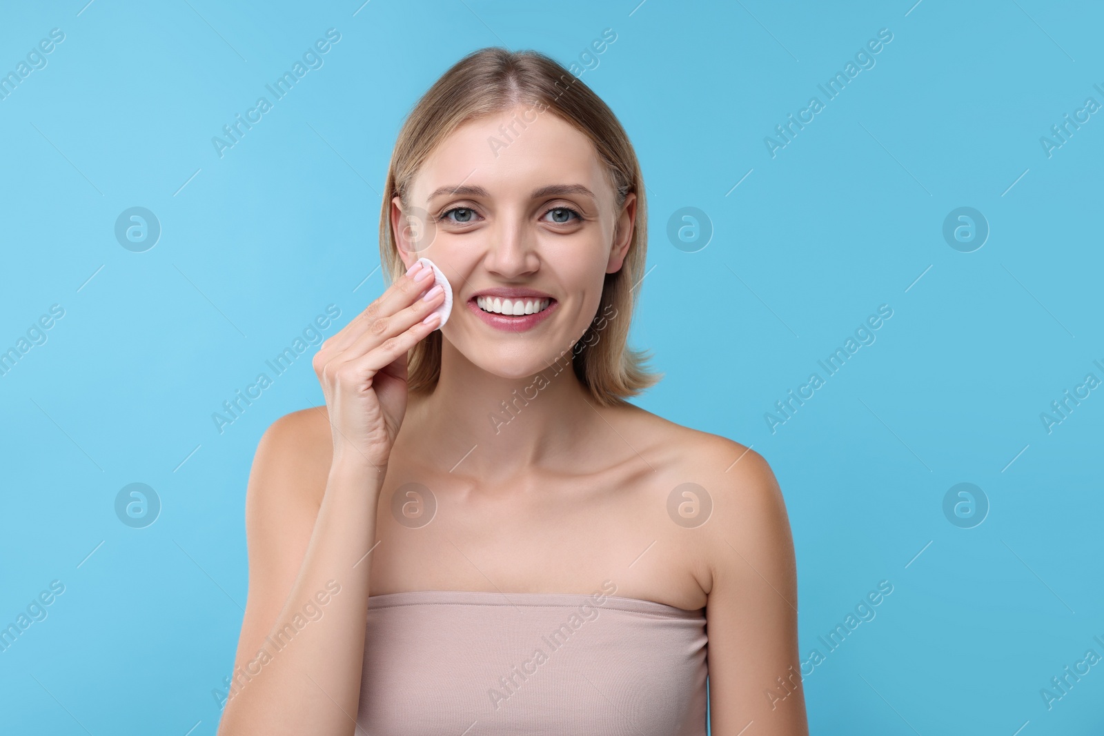 Photo of Young woman cleaning face with cotton pad on light blue background